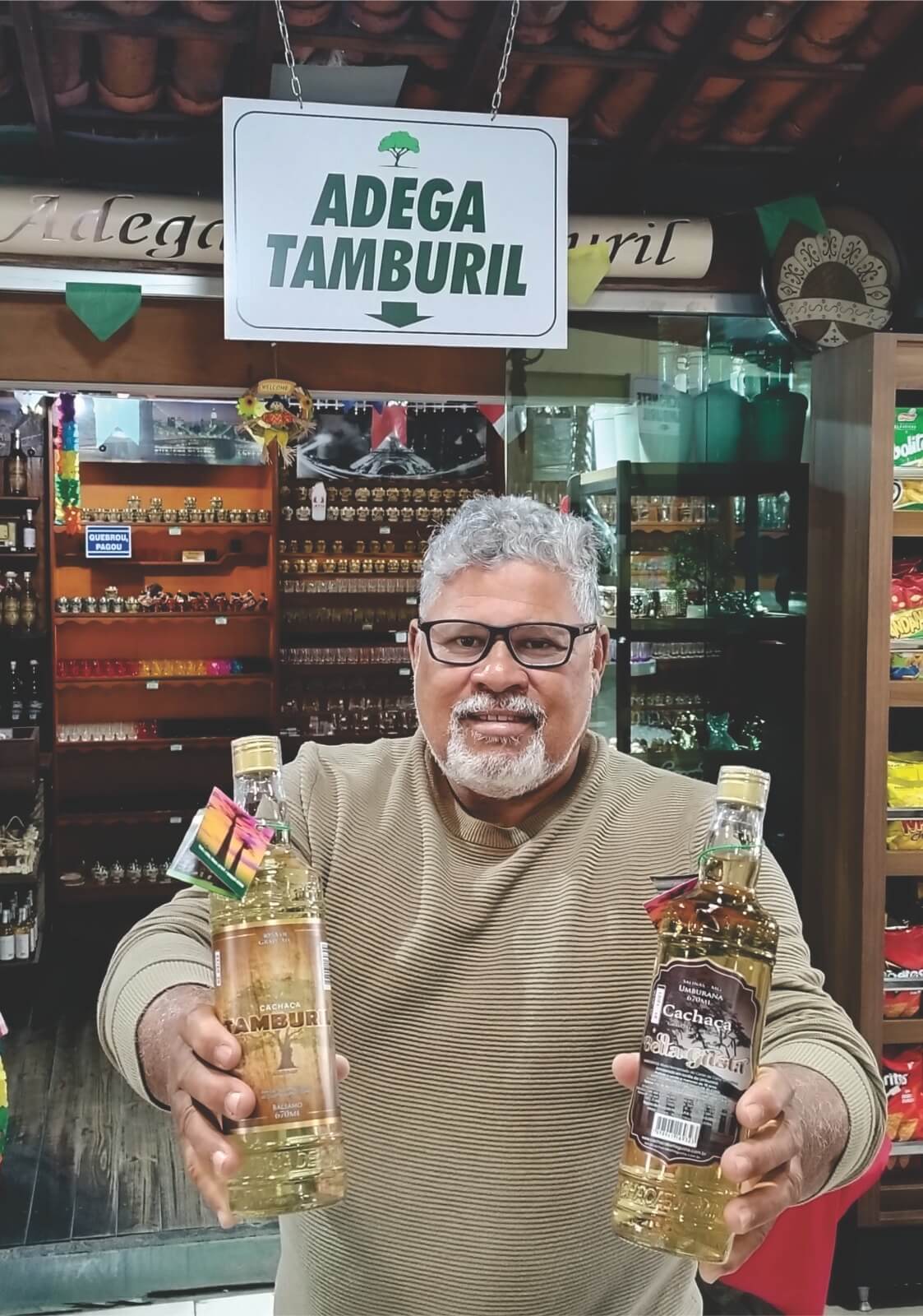 Jornalista Aurélio Vidal segurando duas garrafas de cachaça na adega Tamburil